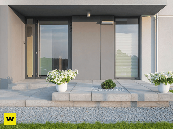 Moderner Hauseingang mit großen Fenstern, Betonplatten und dekorativen Blumenkübeln.