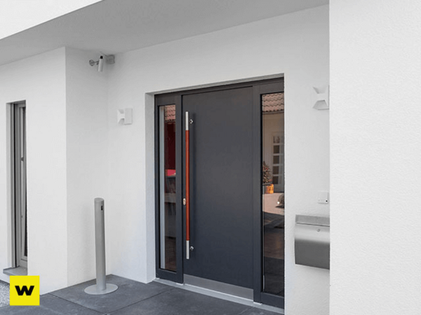 Moderne Haustür aus dunklem Metall mit Glaseinsatz an weißer Fassade und Briefkasten.