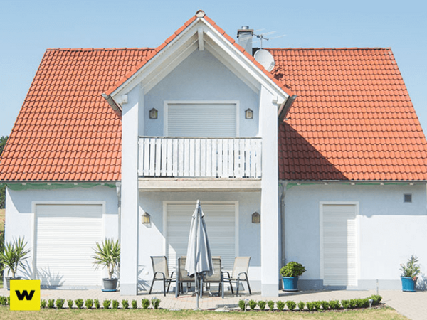 Modernes Einfamilienhaus mit rotem Dach, Rollläden und Terrasse bei sonnigem Wetter.